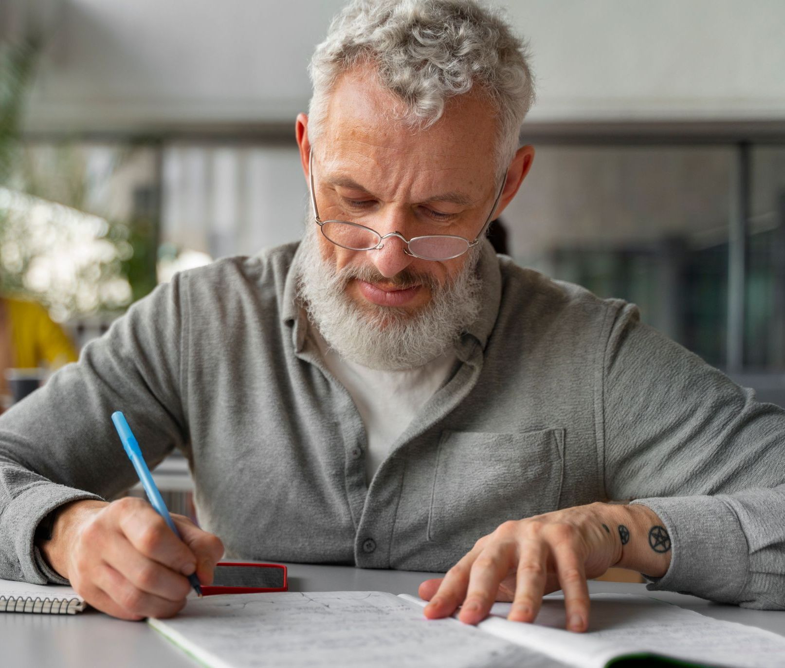 A man with a beard is sitting at a table writing in a notebook.