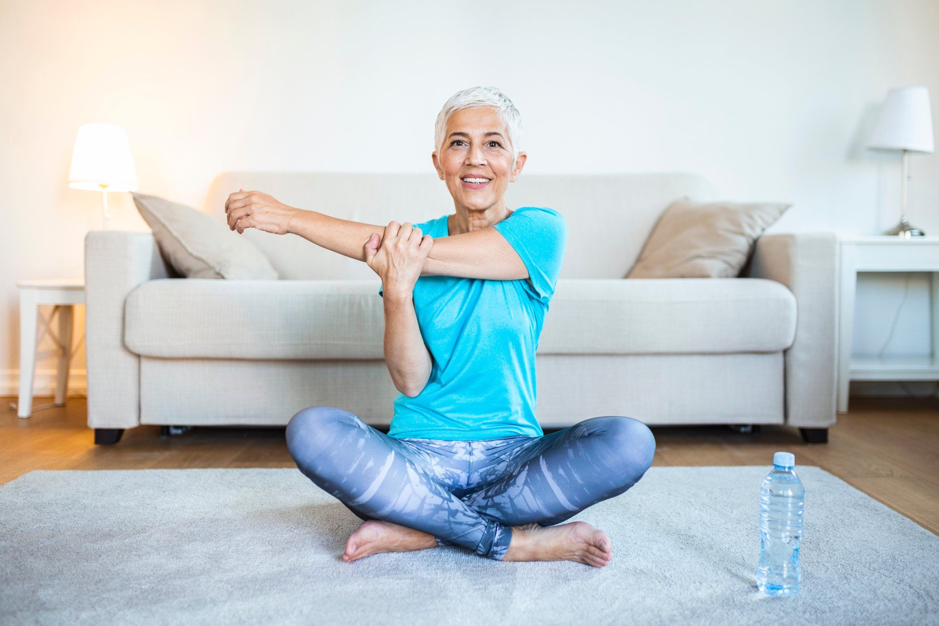 A woman is sitting on the floor stretching her arms in a living room.