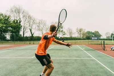 A man in an orange shirt is playing tennis on a tennis court.