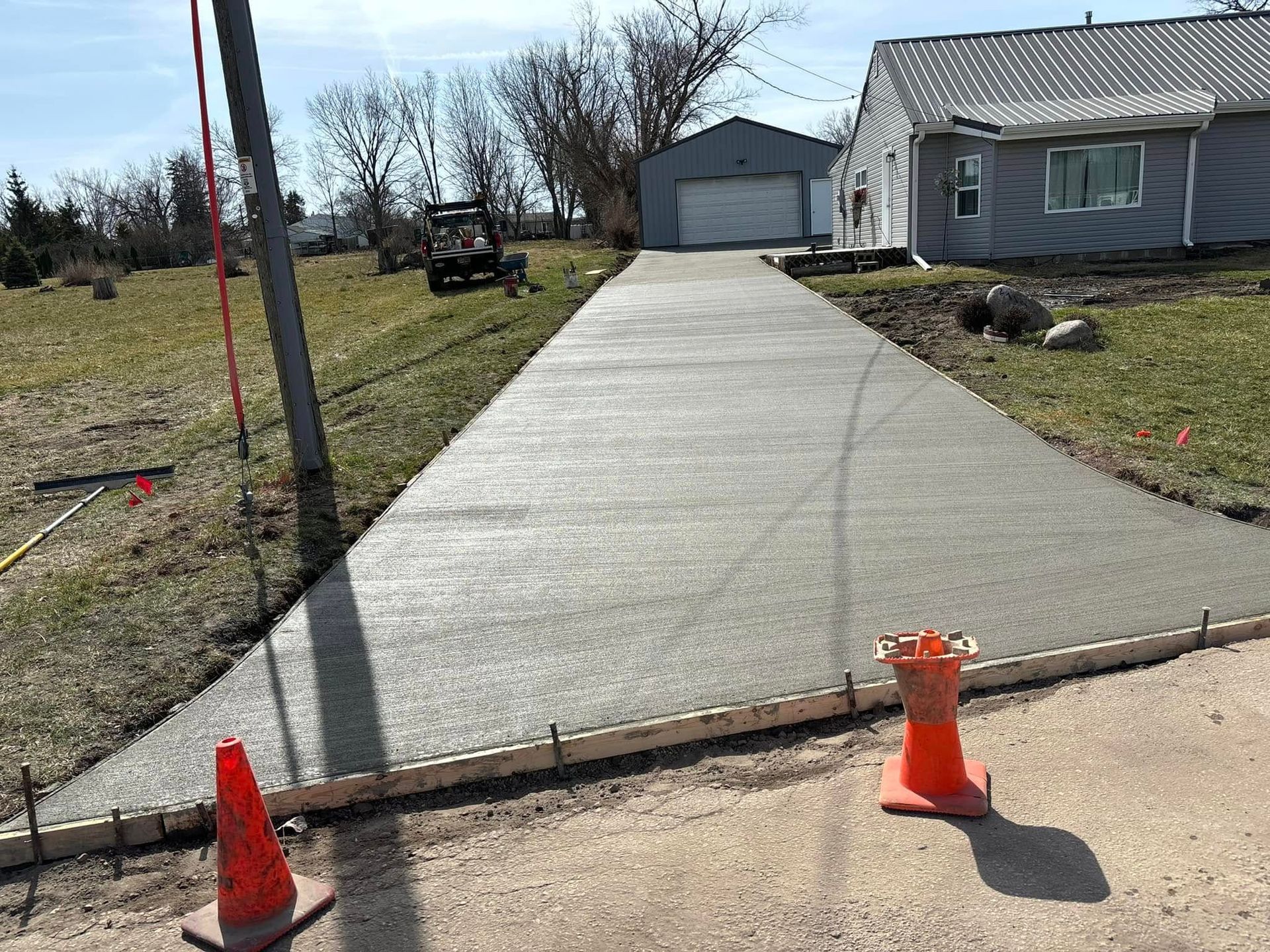Newly poured concrete driveway with orange safety cones; home and garage in the background.