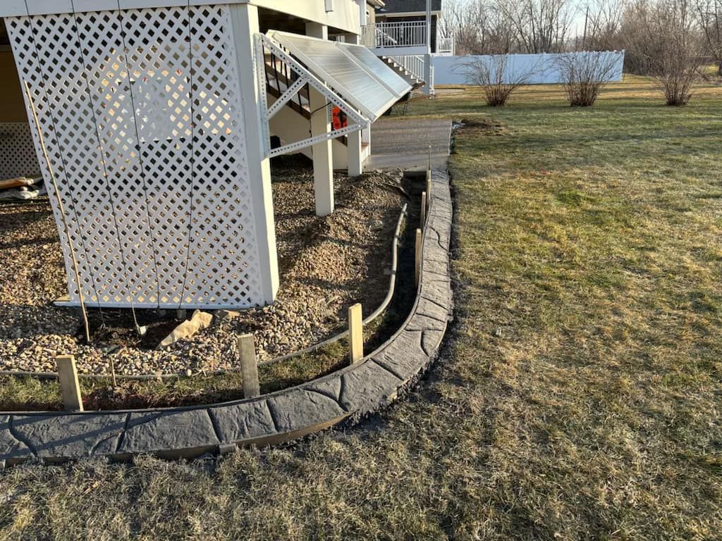 Gray stone border outlines a curved walkway next to a white deck, set in a grassy yard.