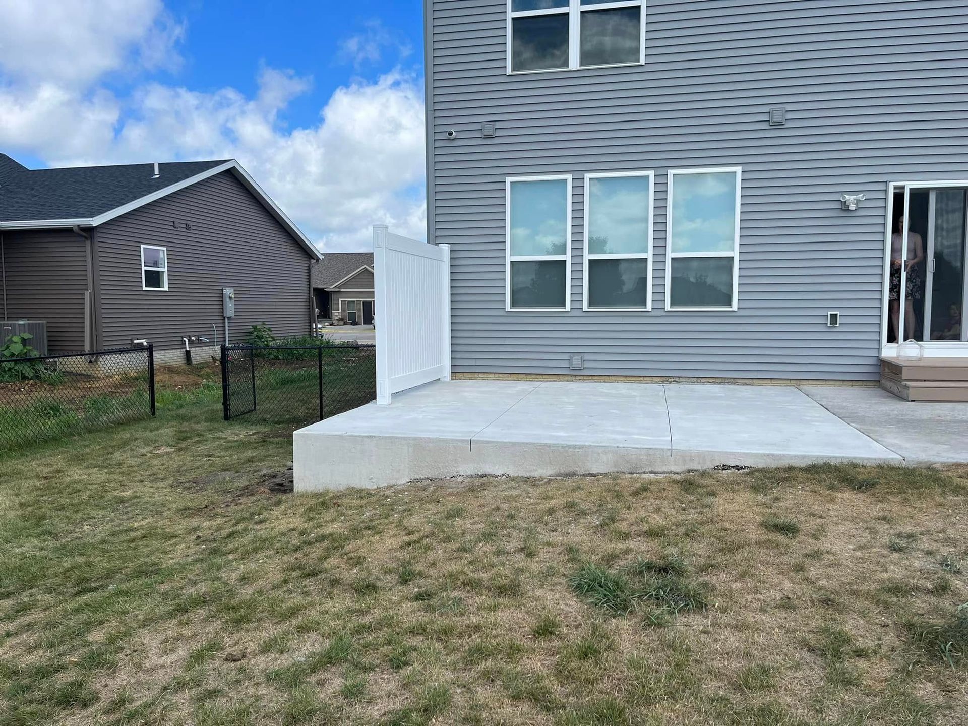 Backyard with concrete patio, gray house with windows, and white fence.