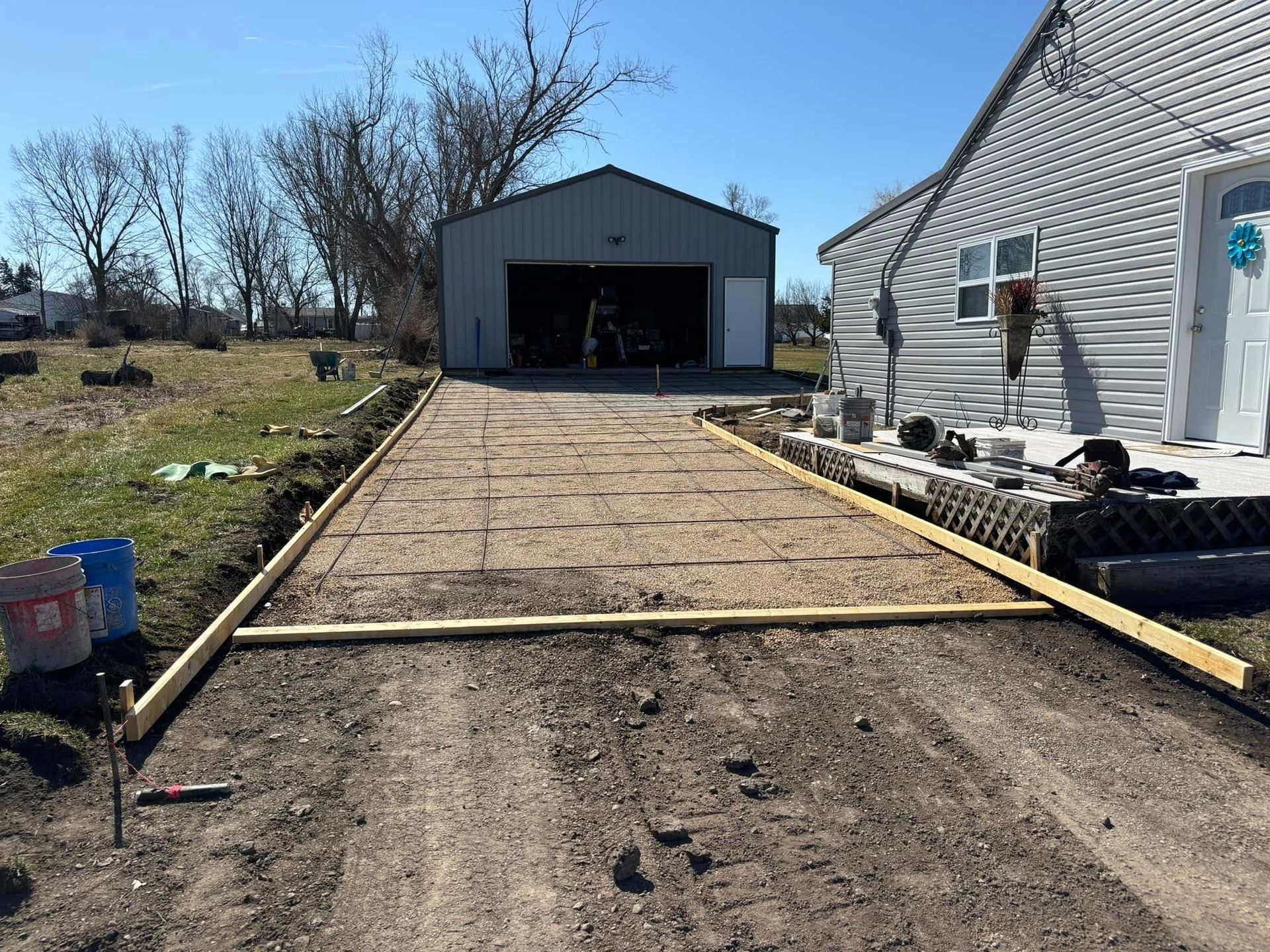 Driveway under construction: wood frame, gravel, garage in background, house to the right. Sunny day.