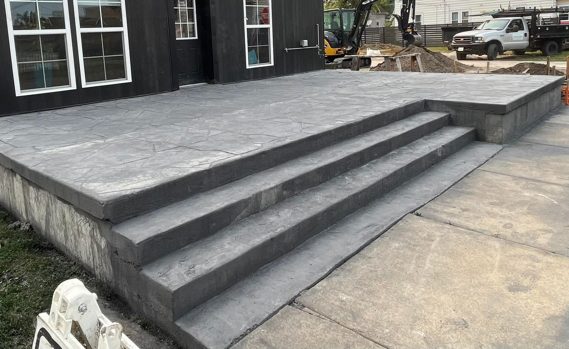 Gray concrete steps leading up to a concrete patio outside a black building.