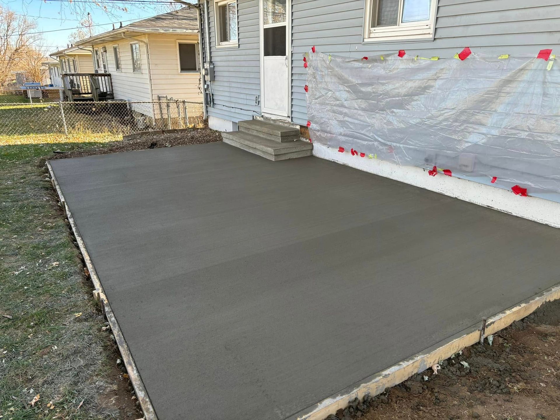Newly poured concrete patio next to a house with a white door and steps.