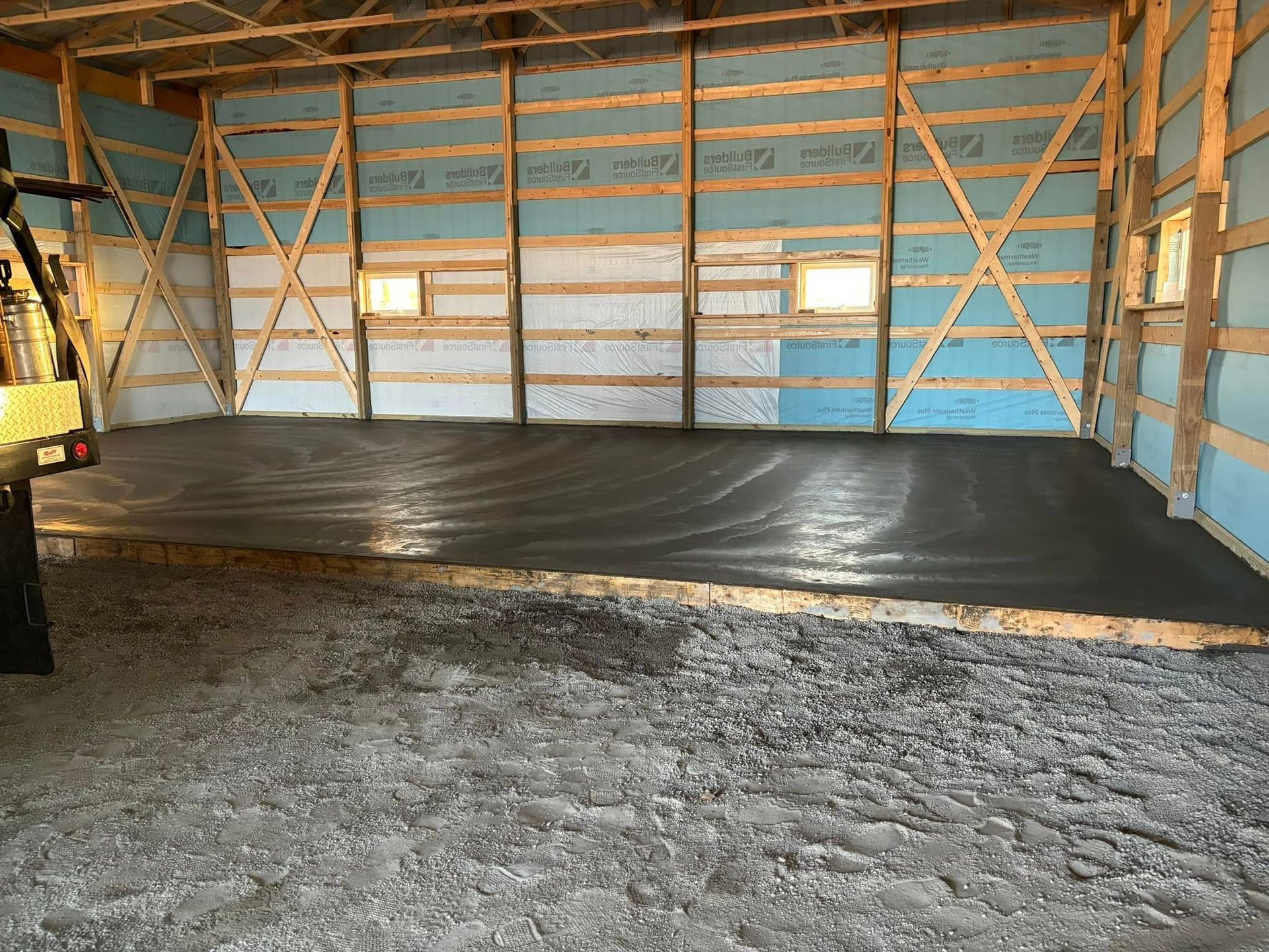 Interior of a wooden framed building with fresh concrete floor. Blue insulation is visible on walls.