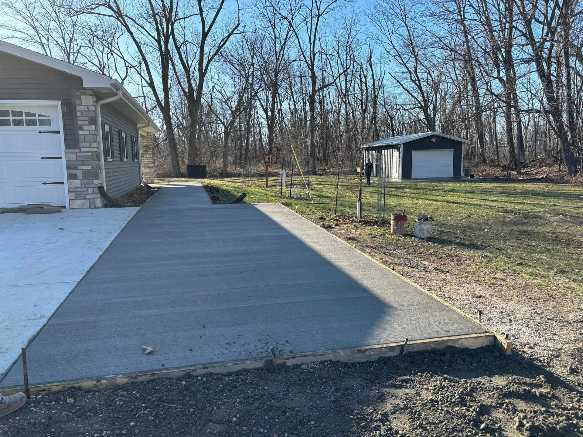 Concrete driveway leads past a house with a garage and to a detached shed on a sunny day.
