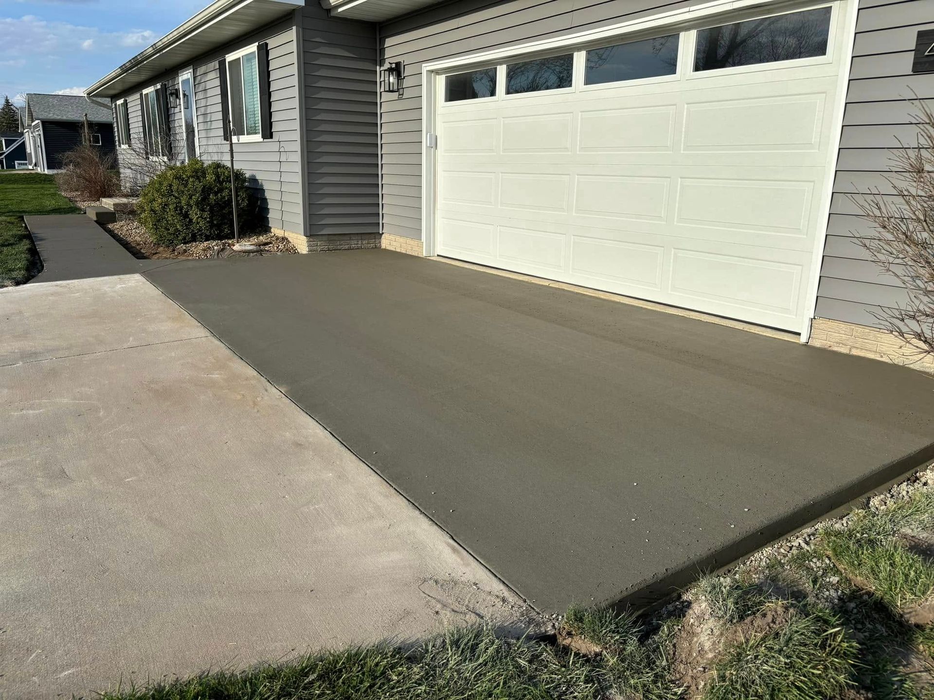 Freshly poured concrete driveway and walkway next to a light-colored garage.