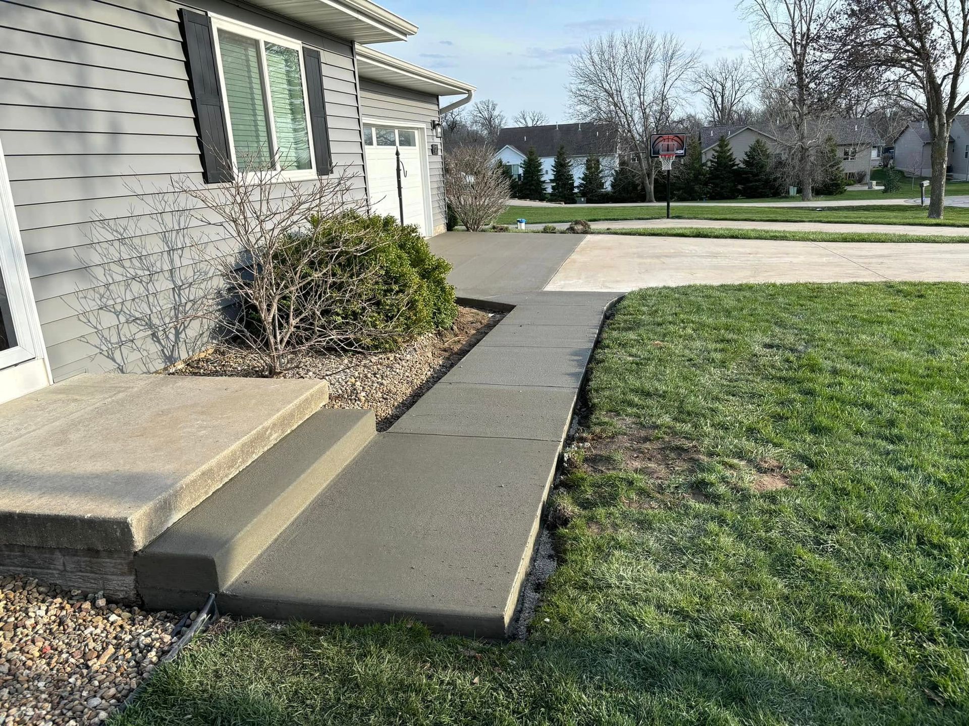 Newly poured concrete walkway and steps leading to a gray house, next to a lawn and driveway.