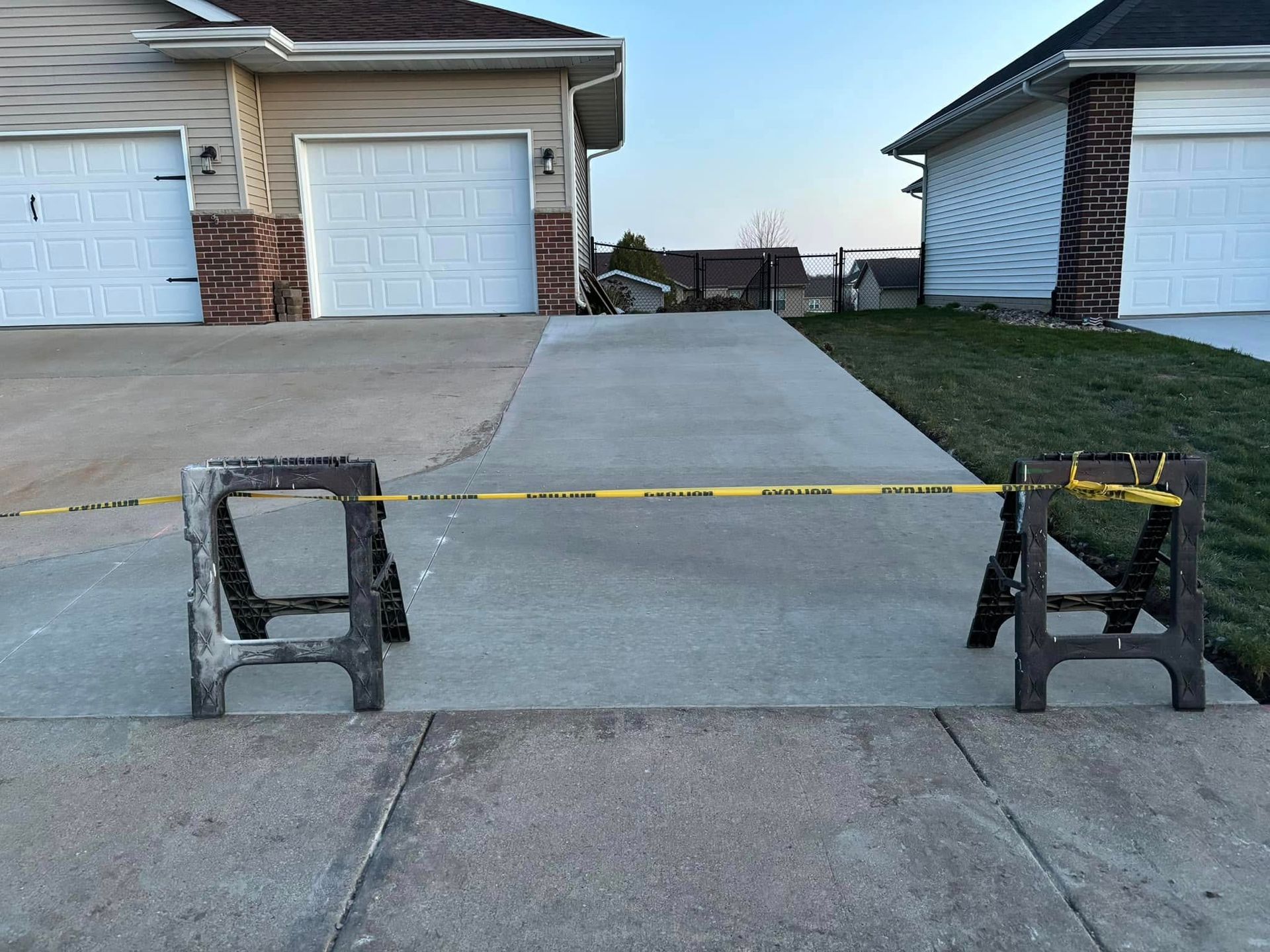 Two sawhorses with yellow caution tape blocking a driveway entrance in front of two houses.
