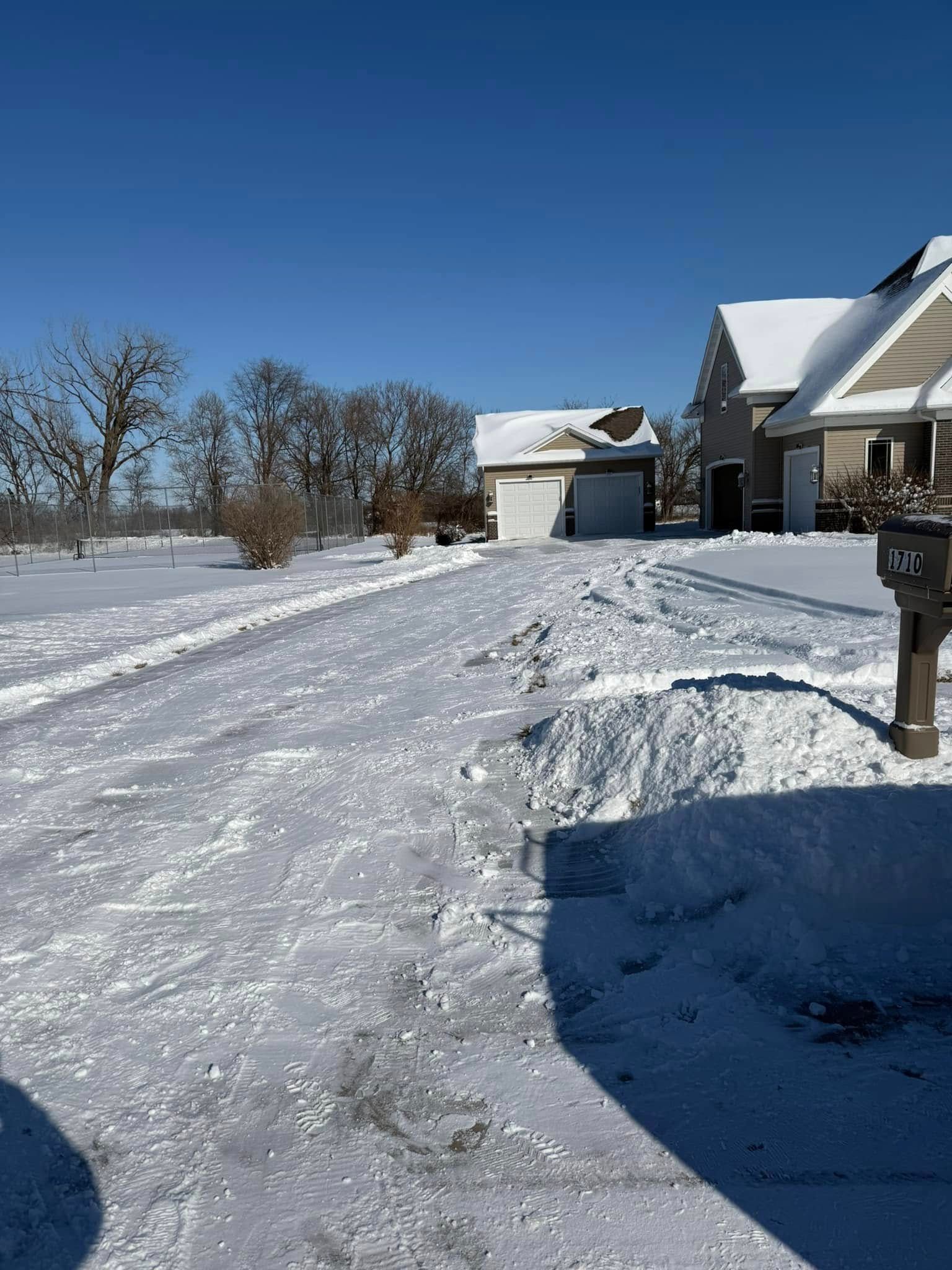 Snow-covered driveway leading to a house and garage; sunny winter day.