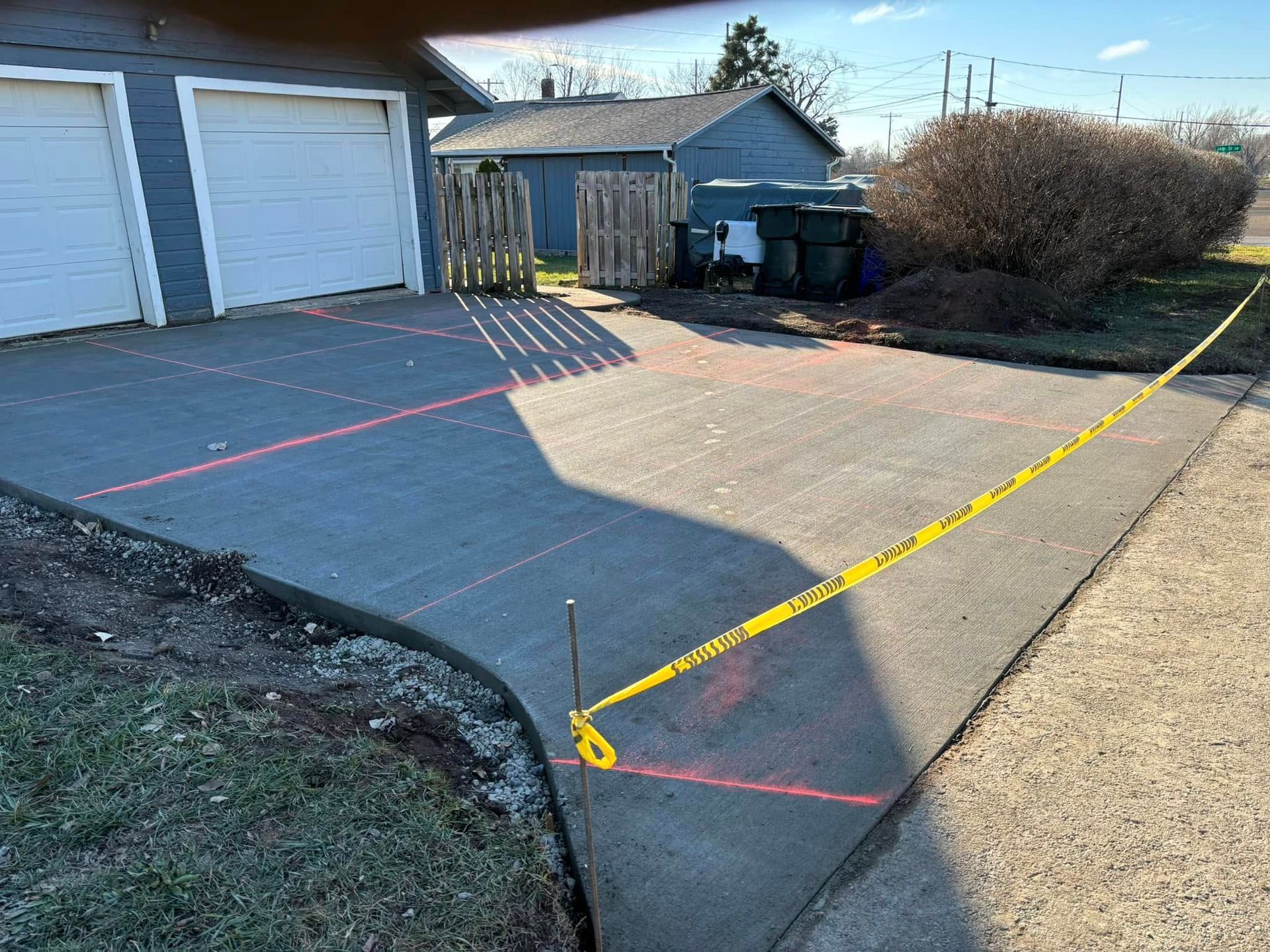 Newly poured concrete driveway with red lines and yellow caution tape. Garage in background.