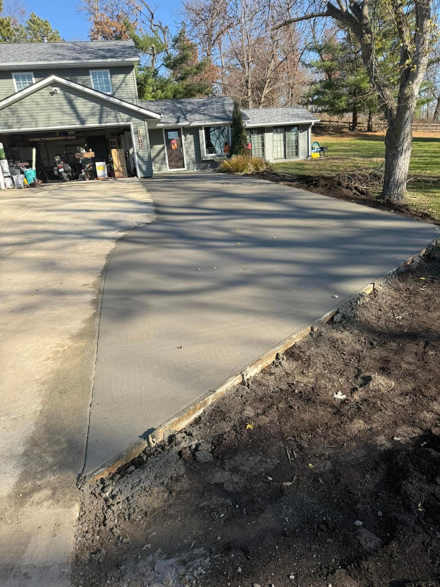 Driveway of a two-story home, freshly poured concrete. Dirt border alongside.