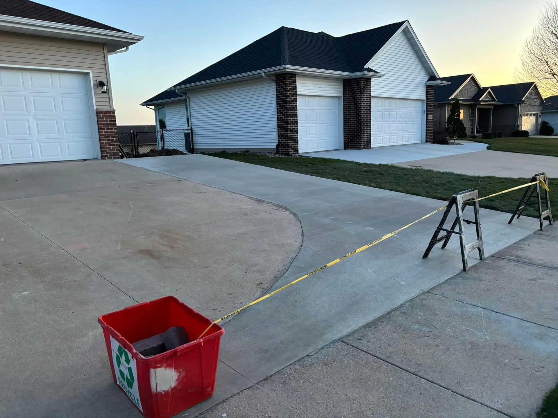 A red recycling bin on a driveway is roped off with caution tape near houses.