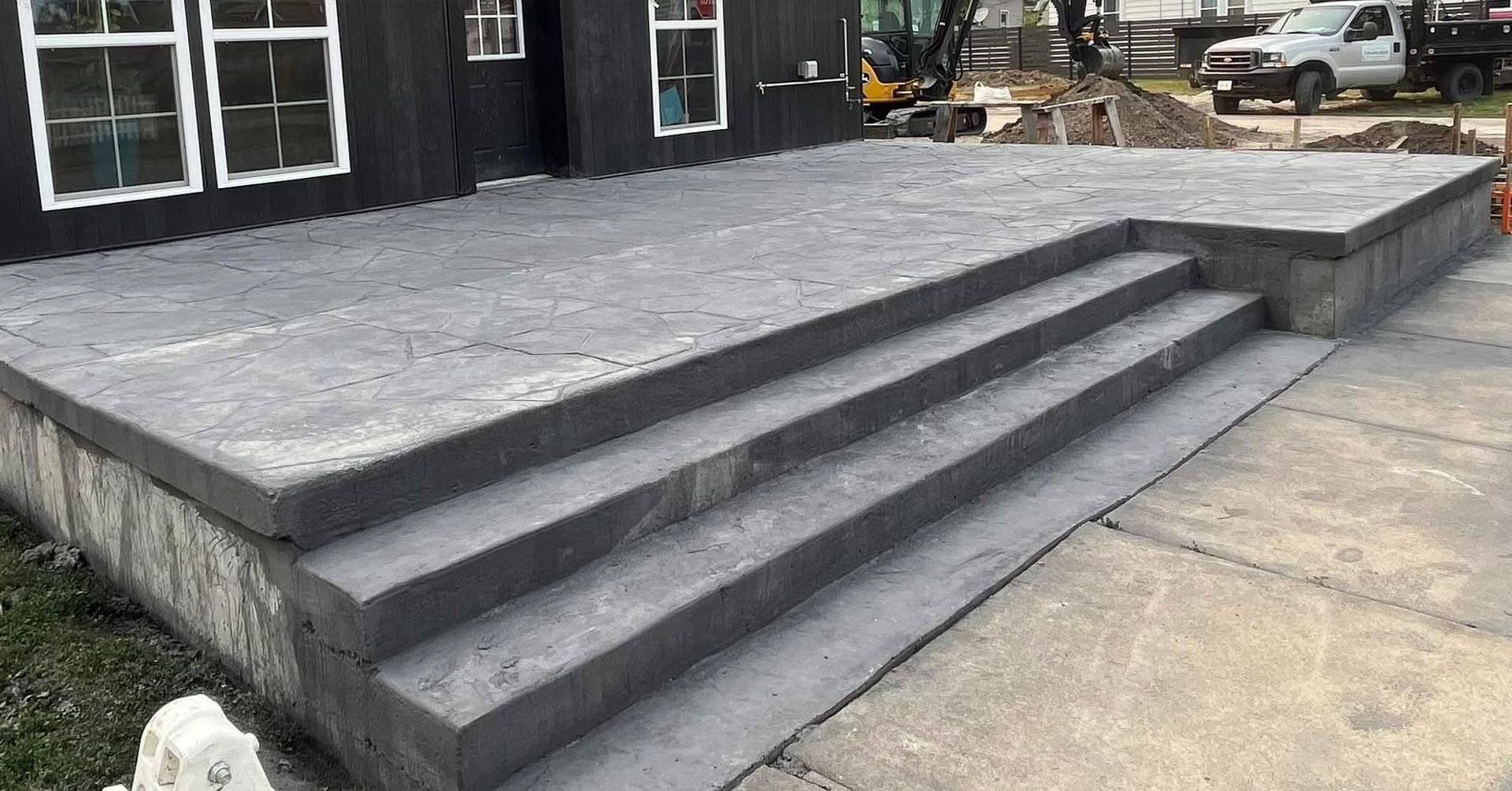Concrete porch with steps leading down to a concrete sidewalk. The house is painted black.