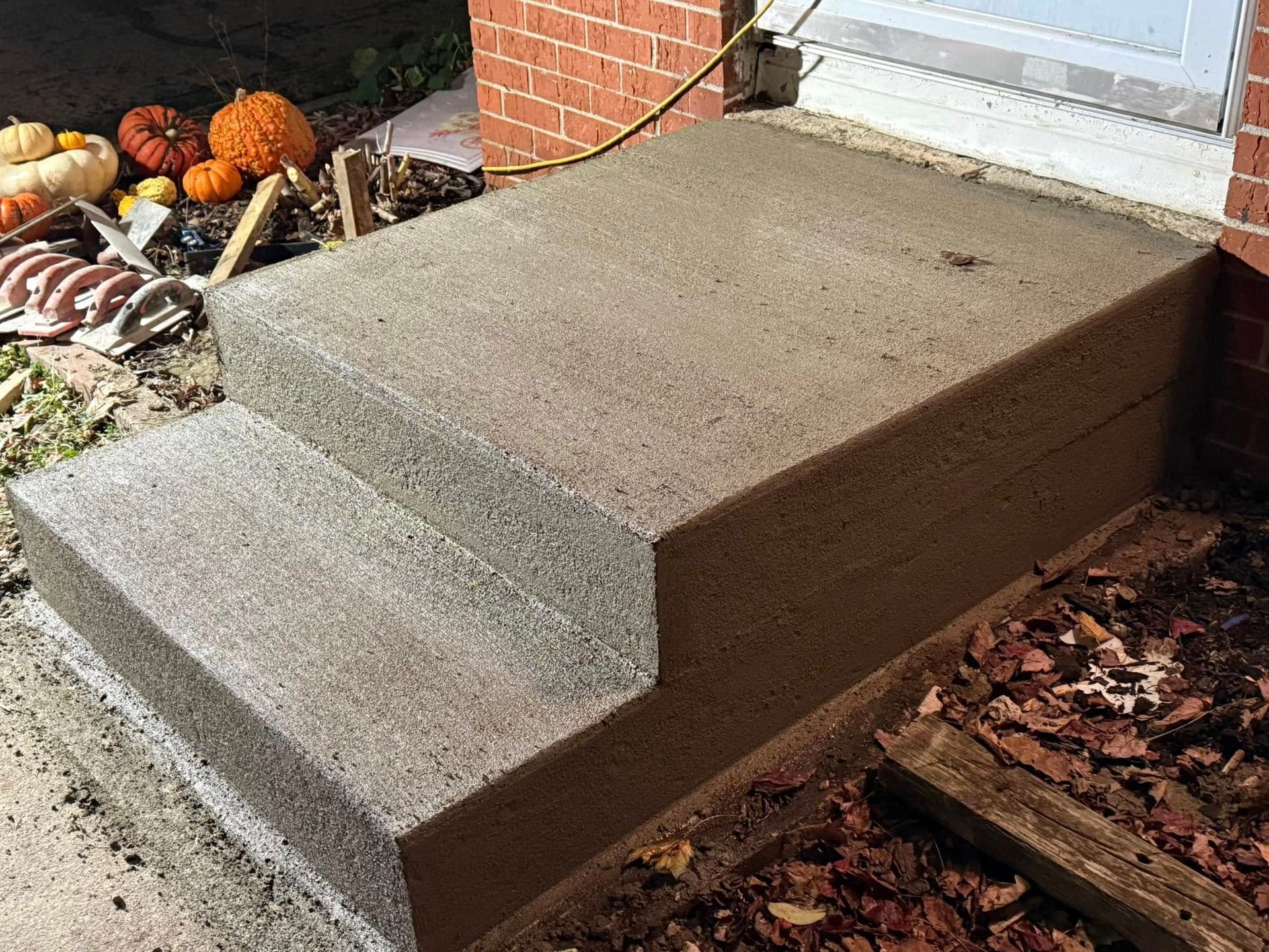 Newly poured concrete steps in front of a brick building, pumpkins and foliage present.