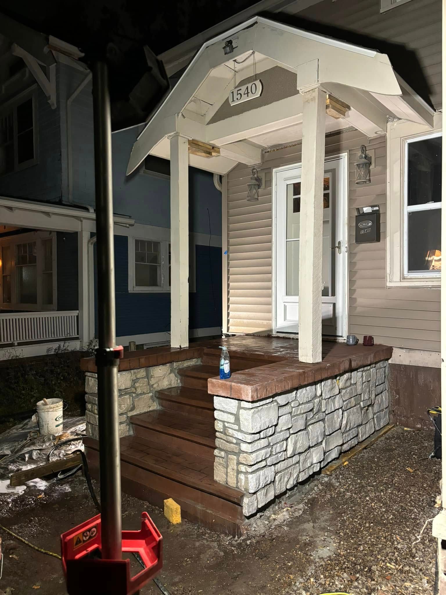 Front porch with stone base, wooden steps, and covered entrance to a house. House number 