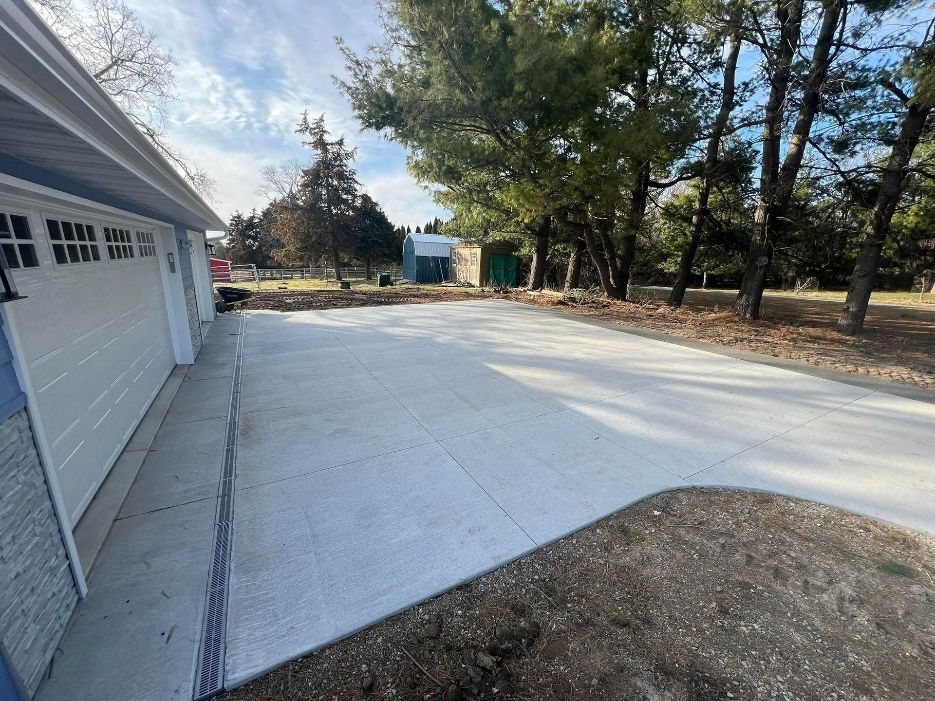 New concrete driveway next to a white garage, with trees in the background under a blue sky.