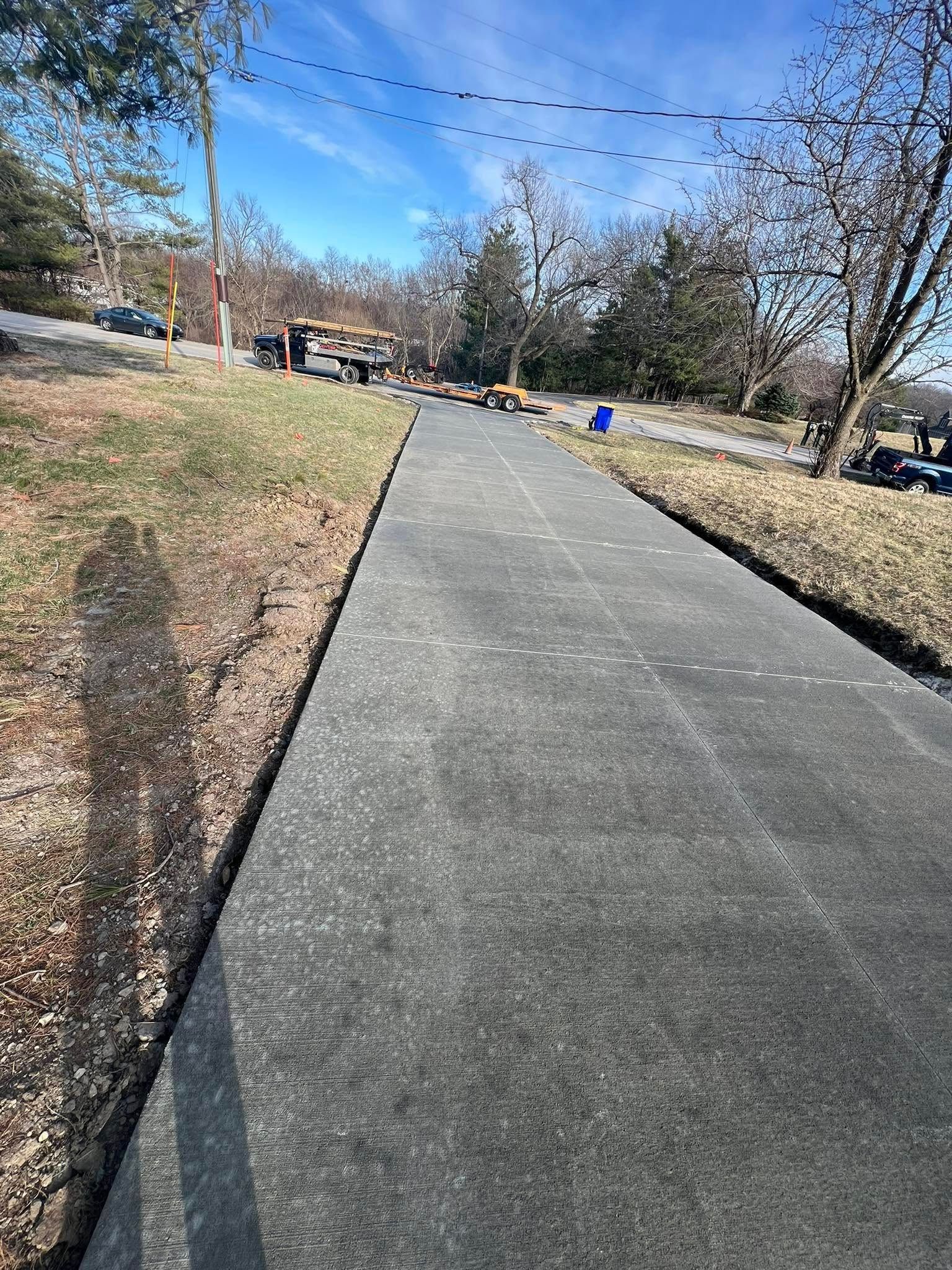 Asphalt pathway with construction equipment and a grassy hillside. Blue sky overhead.