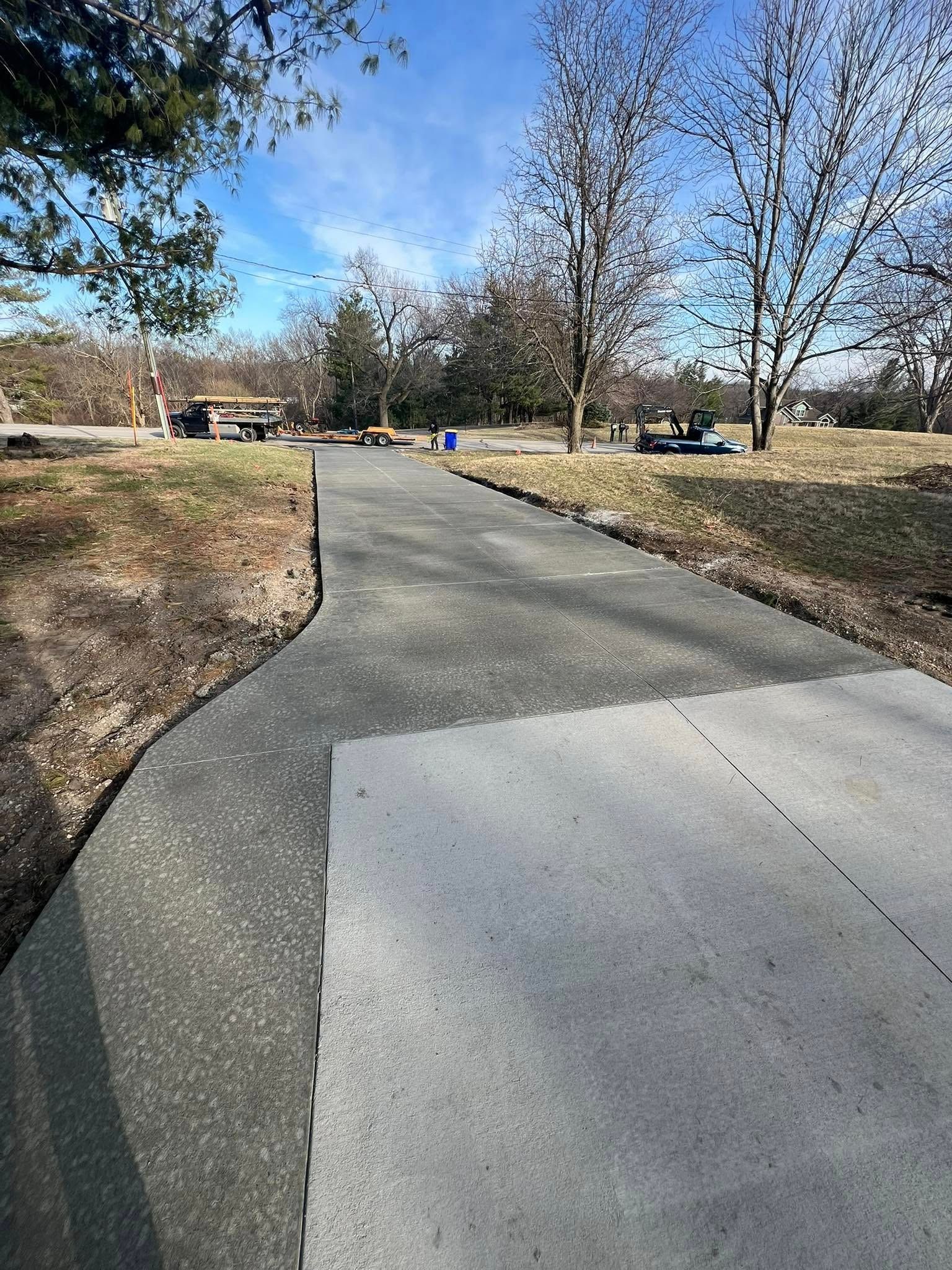 Paved path curves through a park with bare trees. A concrete slab is at the bottom. Blue sky.