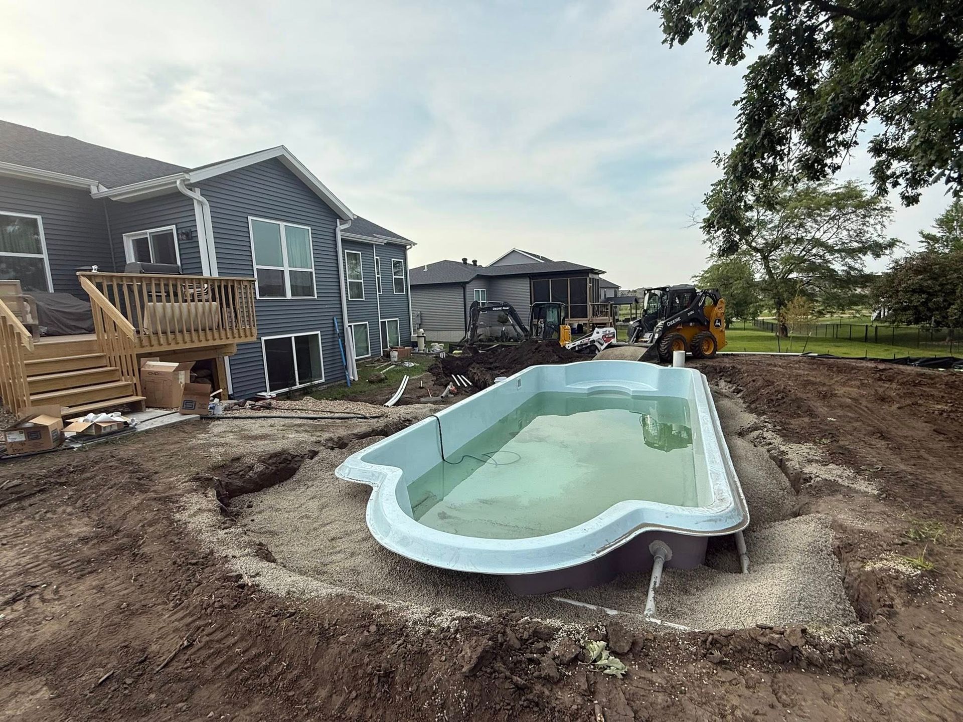 Newly installed swimming pool in backyard excavation, near house and construction.