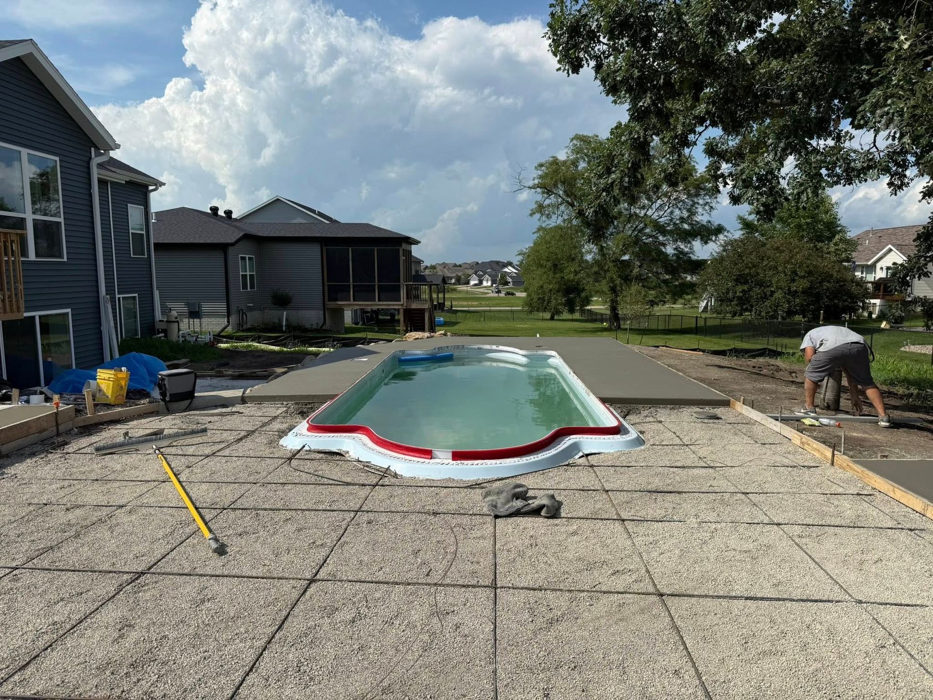 Pool construction: A partially built pool surrounded by concrete forms, a worker, and houses in the background.