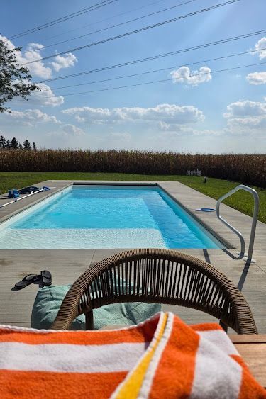 Pool with clear blue water on a sunny day. A deck chair and striped towel are in the foreground.