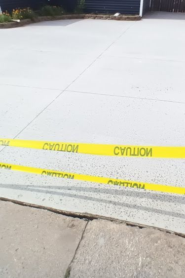 Yellow caution tape stretches across a concrete driveway.