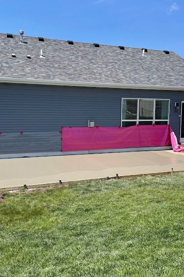Pink tarp draped along the side of a blue house with a concrete patio and green lawn.