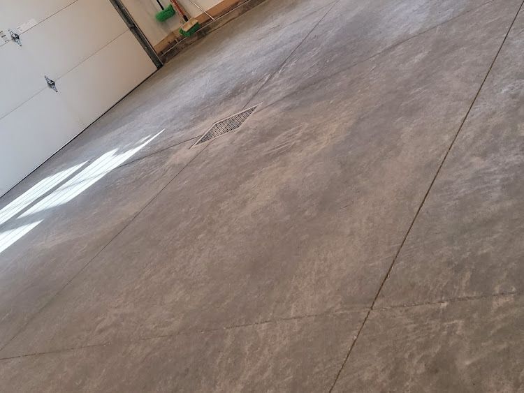 Concrete garage floor, partially lit, with seams and a drain.