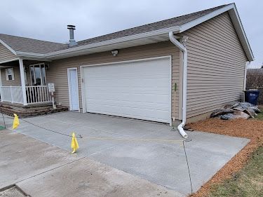Garage of a house with a white door, concrete driveway, and brown siding.