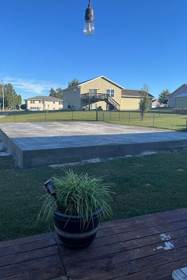 A concrete slab in a backyard with grass, a house in the background, and a hanging light bulb.