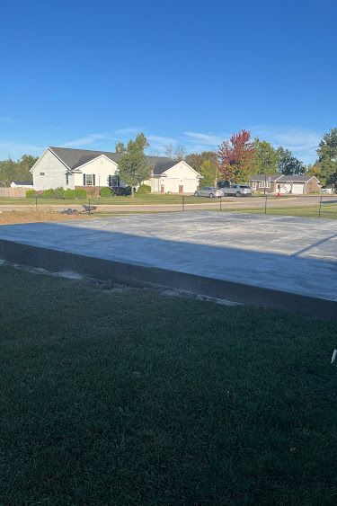 Concrete slab in front of a grassy yard with houses and a clear blue sky in the background.