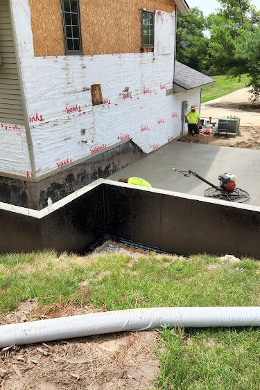 Construction workers pouring and smoothing concrete patio next to a house with exposed siding.