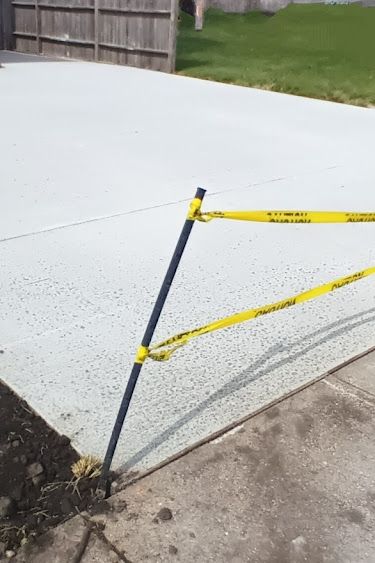 Freshly poured concrete driveway with yellow caution tape attached to a black post.