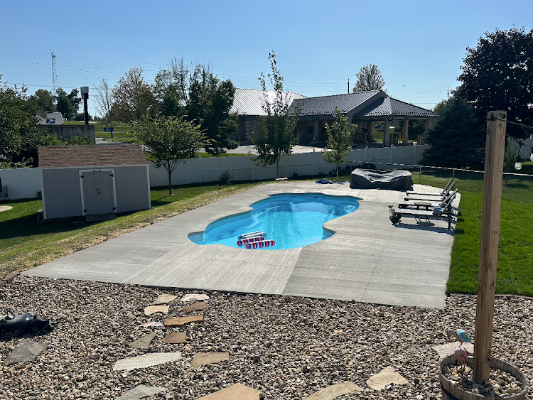 Backyard with a blue swimming pool, concrete patio, lawn, and gravel. A gazebo is in the background.