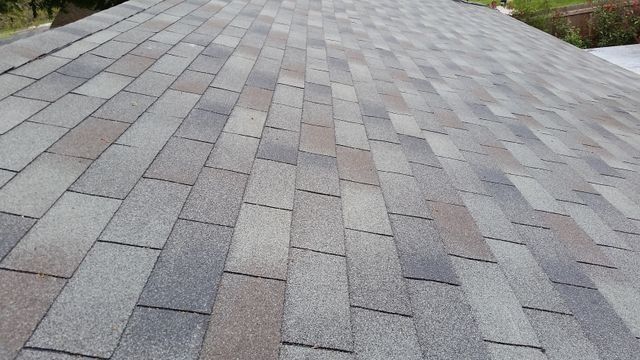 Close-up of a gray shingle roof with weathered, uneven patches.
