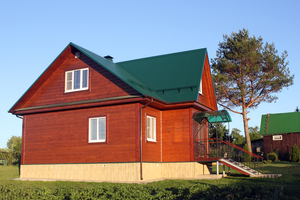 Red wooden house with a green roof on a grassy field under a clear sky