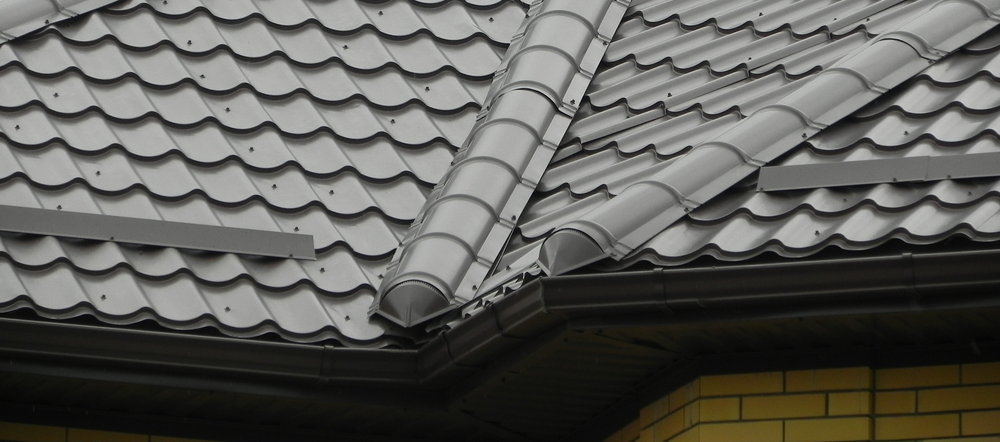 Close-up of gray tiled roof with two curved roof vents and a brick wall edge