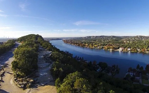 Aerial view of a wide blue river curving through a green residential landscape under a clear sky.
