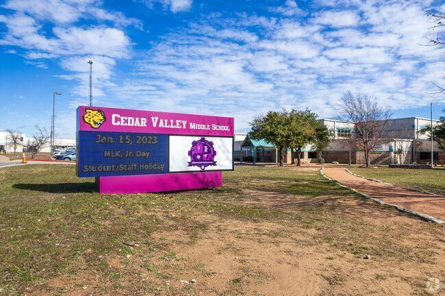 Cedar Valley school sign on a grassy roadside under a blue sky with clouds