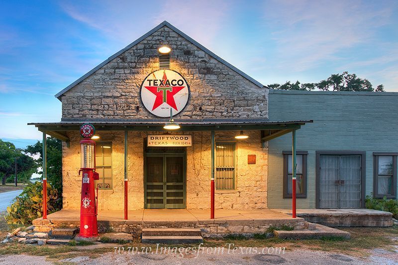 Historic Texaco gas station with stone facade, red pumps, and a large Texaco star sign at dusk