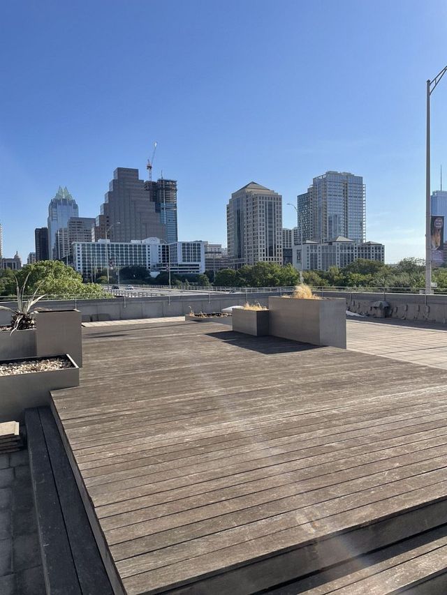 Rooftop wooden deck overlooking a city skyline with several tall buildings under a clear blue sky
