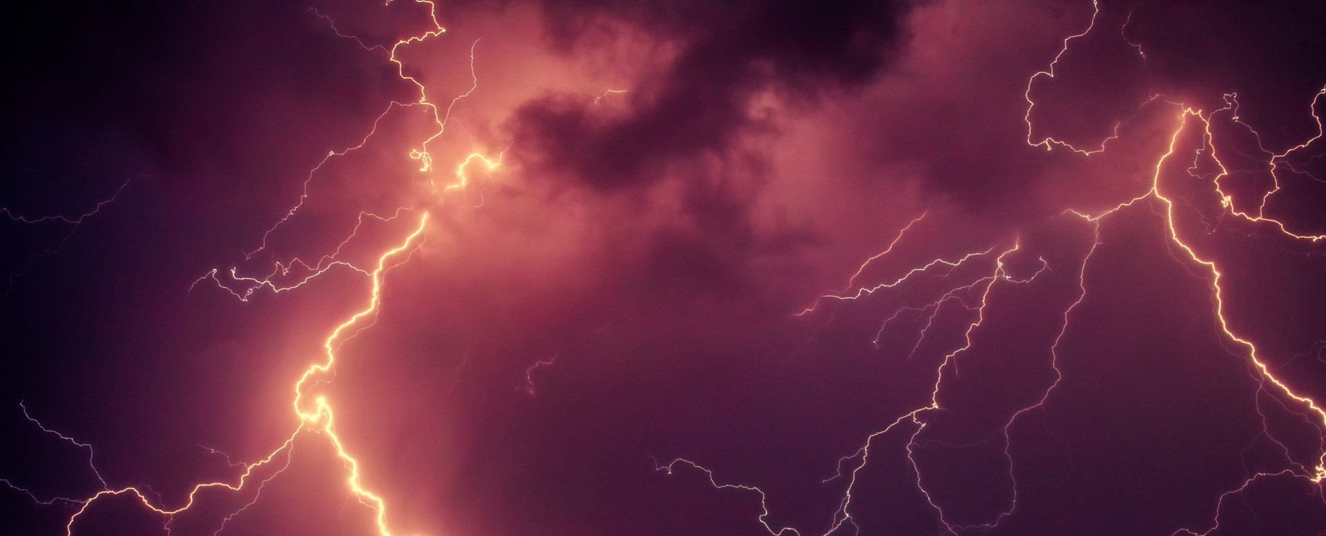 Purple sky lit by bright pink lightning bolts during a storm