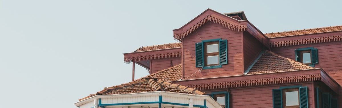 Red shingled building with teal-trimmed windows and ornate roof details against a pale sky