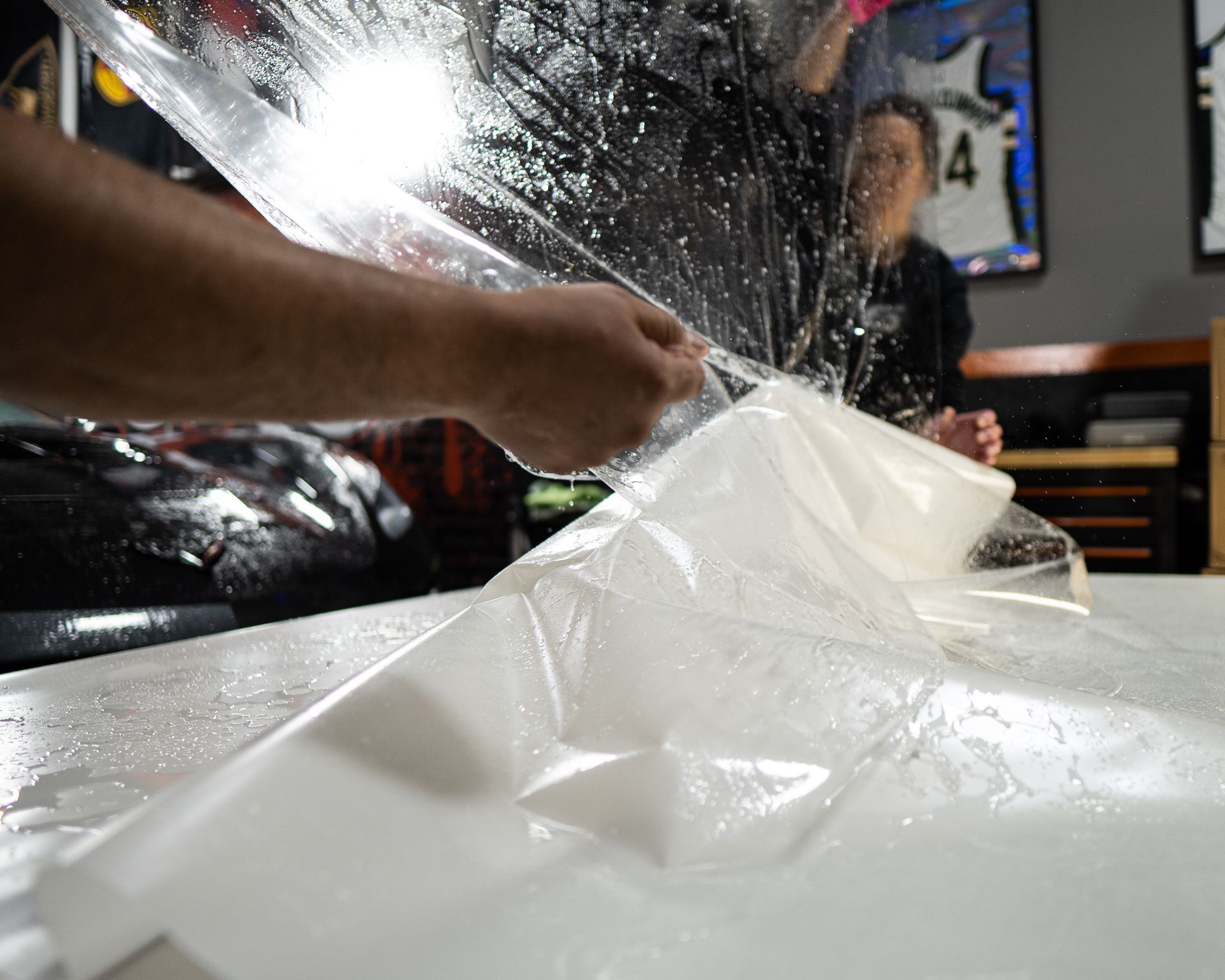 A person is covering a car with plastic wrap.