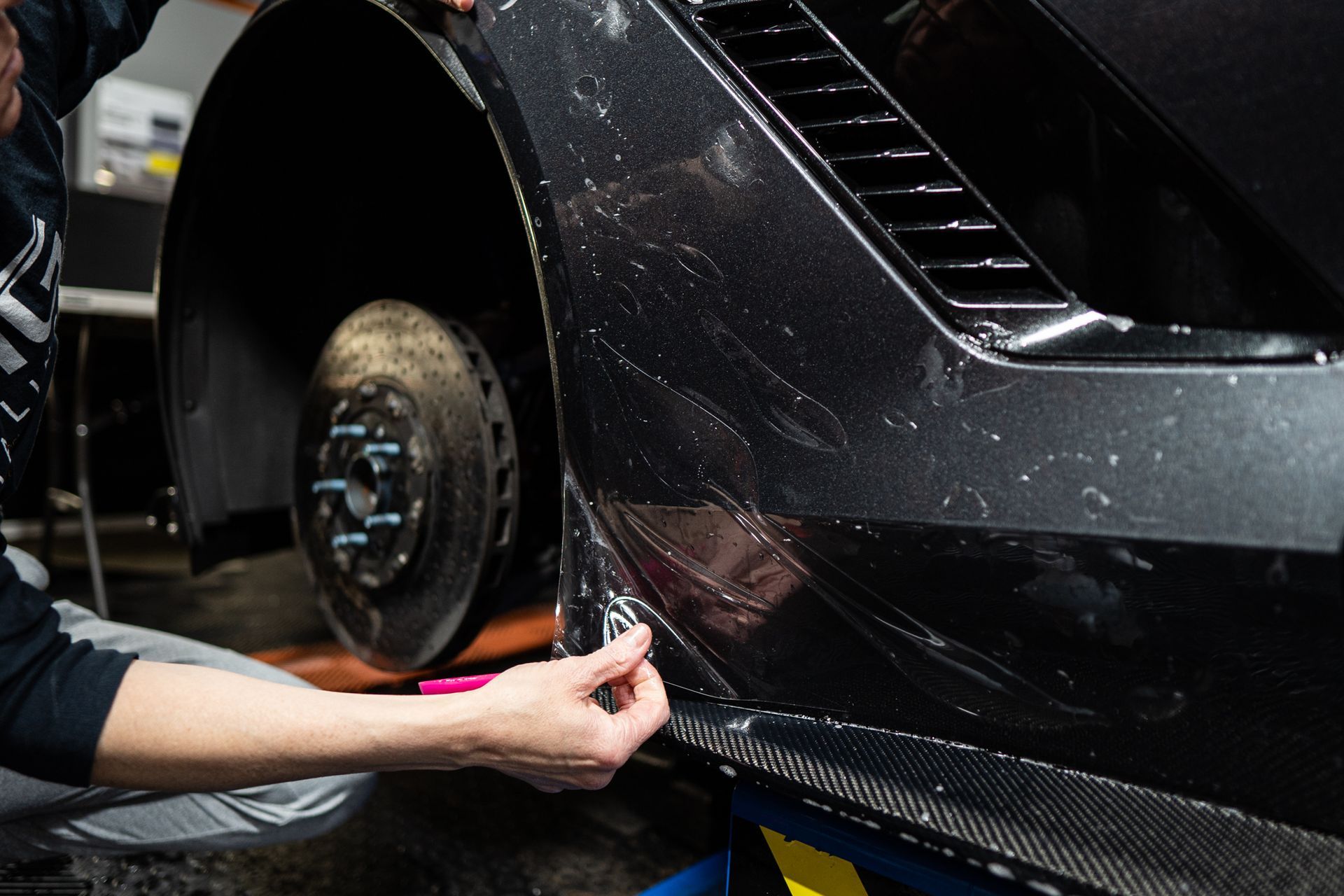 A person is applying a protective film to the side of a car.