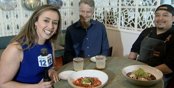 Three people at a restaurant table with plated food, smiling at the camera.