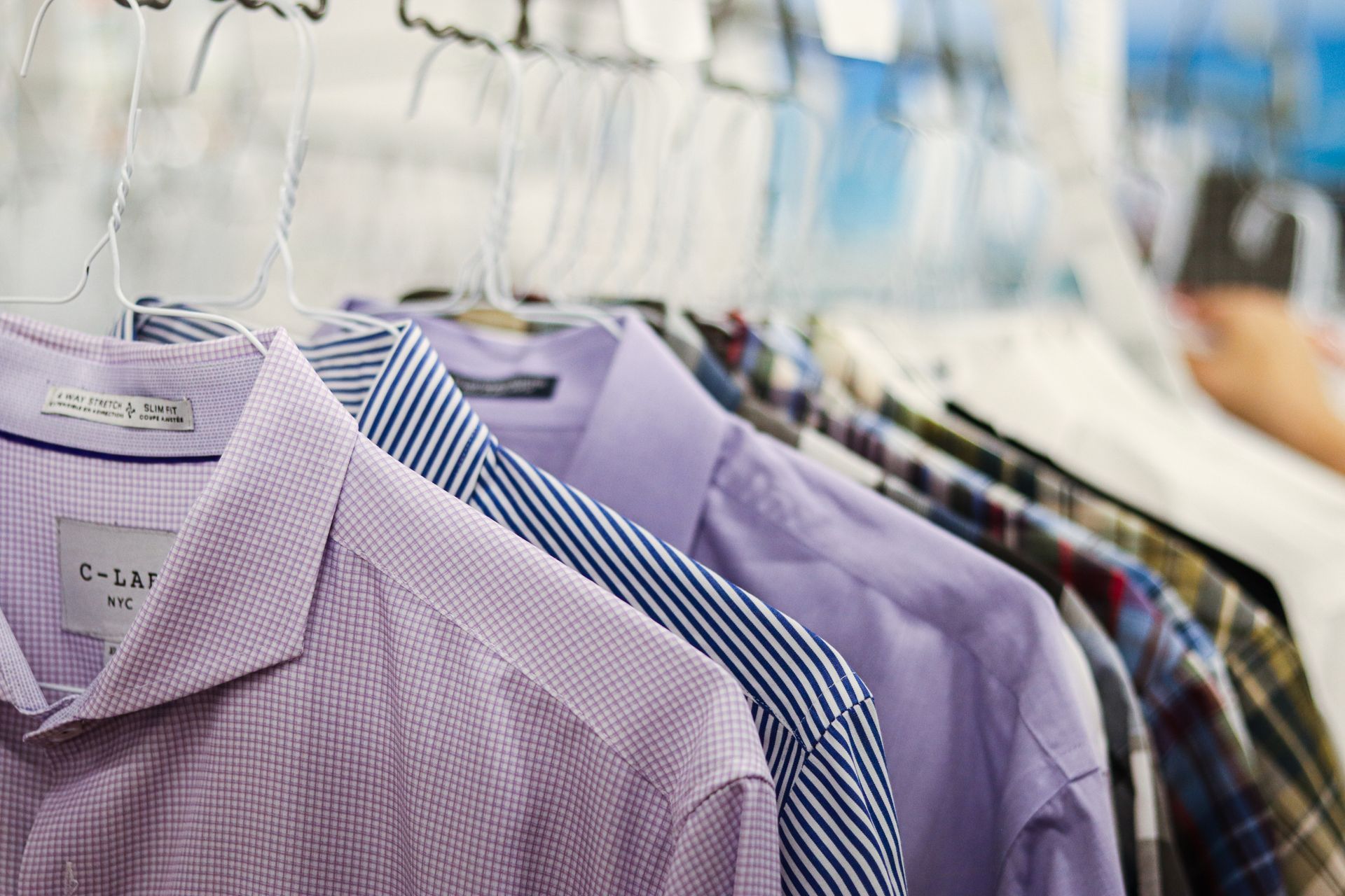 Row of freshly pressed men's shirts on hangers, varying colors including purple and blue.