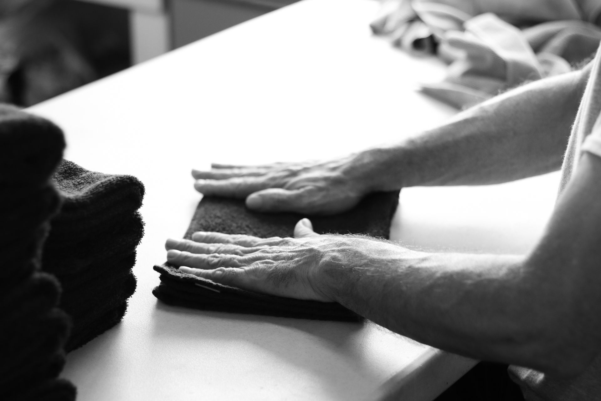 Person folding a dark cloth on a white table, likely for a stack of folded items.